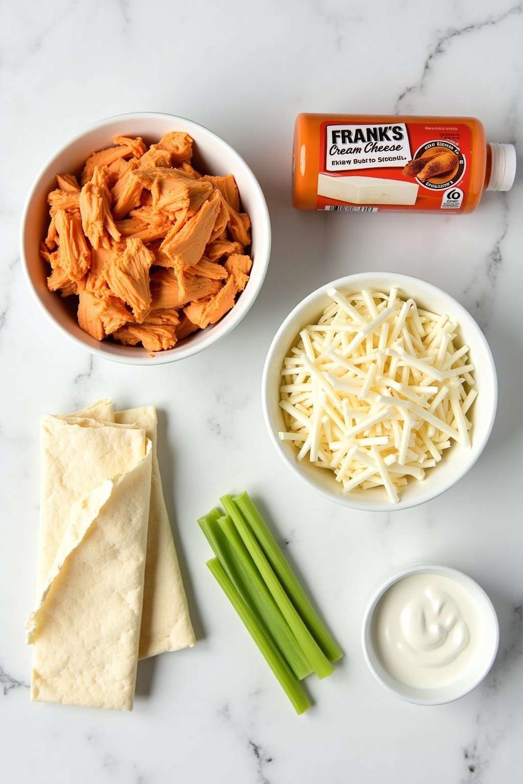 Overhead flat lay of buffalo chicken taquito ingredients: a bowl of shredded chicken, softened cream cheese block, a bottle of Frank's RedHot buffalo sauce, shredded mozzarella, small flour tortill...