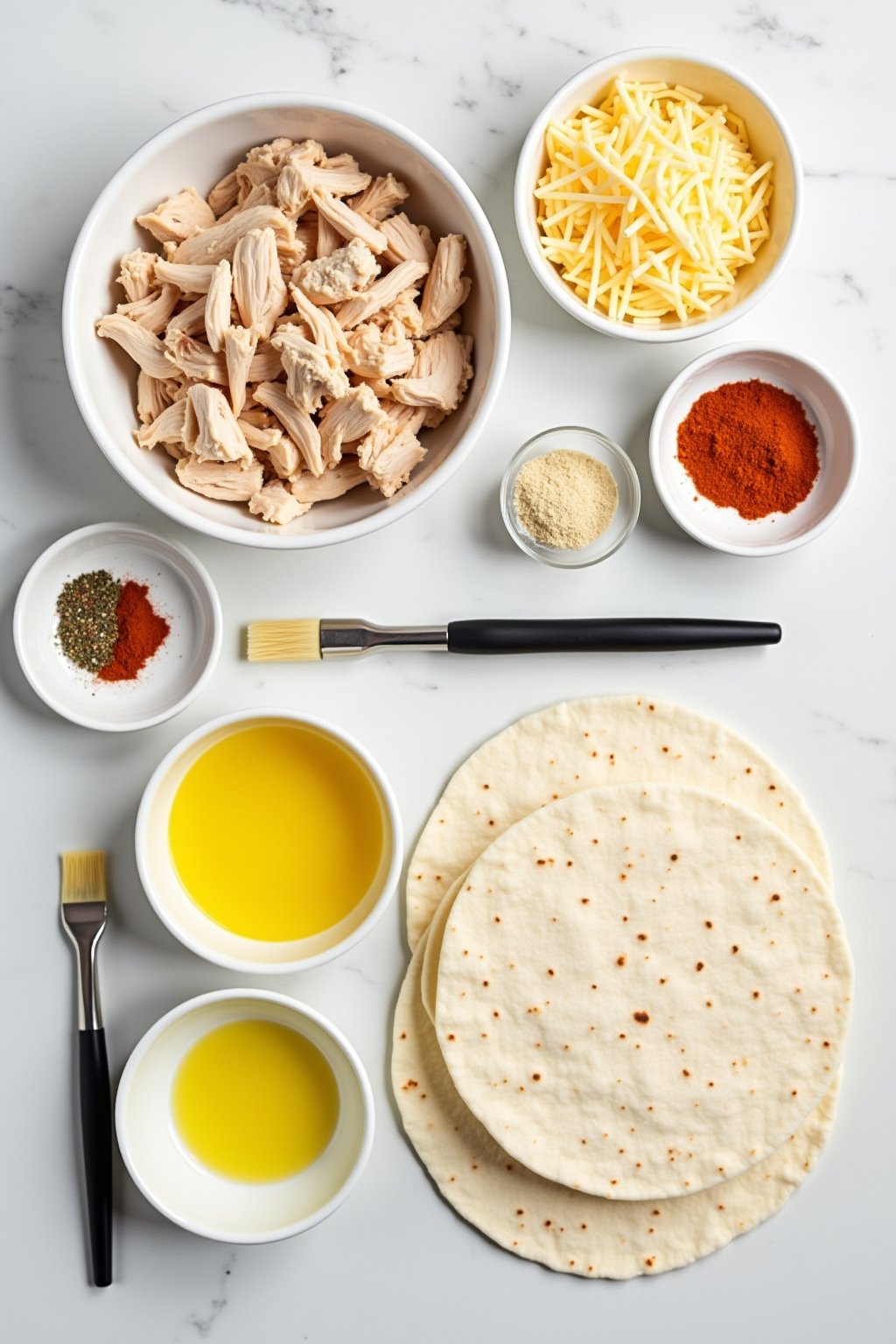 Overhead flat lay of chicken wrap ingredients: a bowl of shredded rotisserie chicken, shredded mozzarella and cheddar in separate bowls, large flour tortillas, melted butter with minced garlic in a...