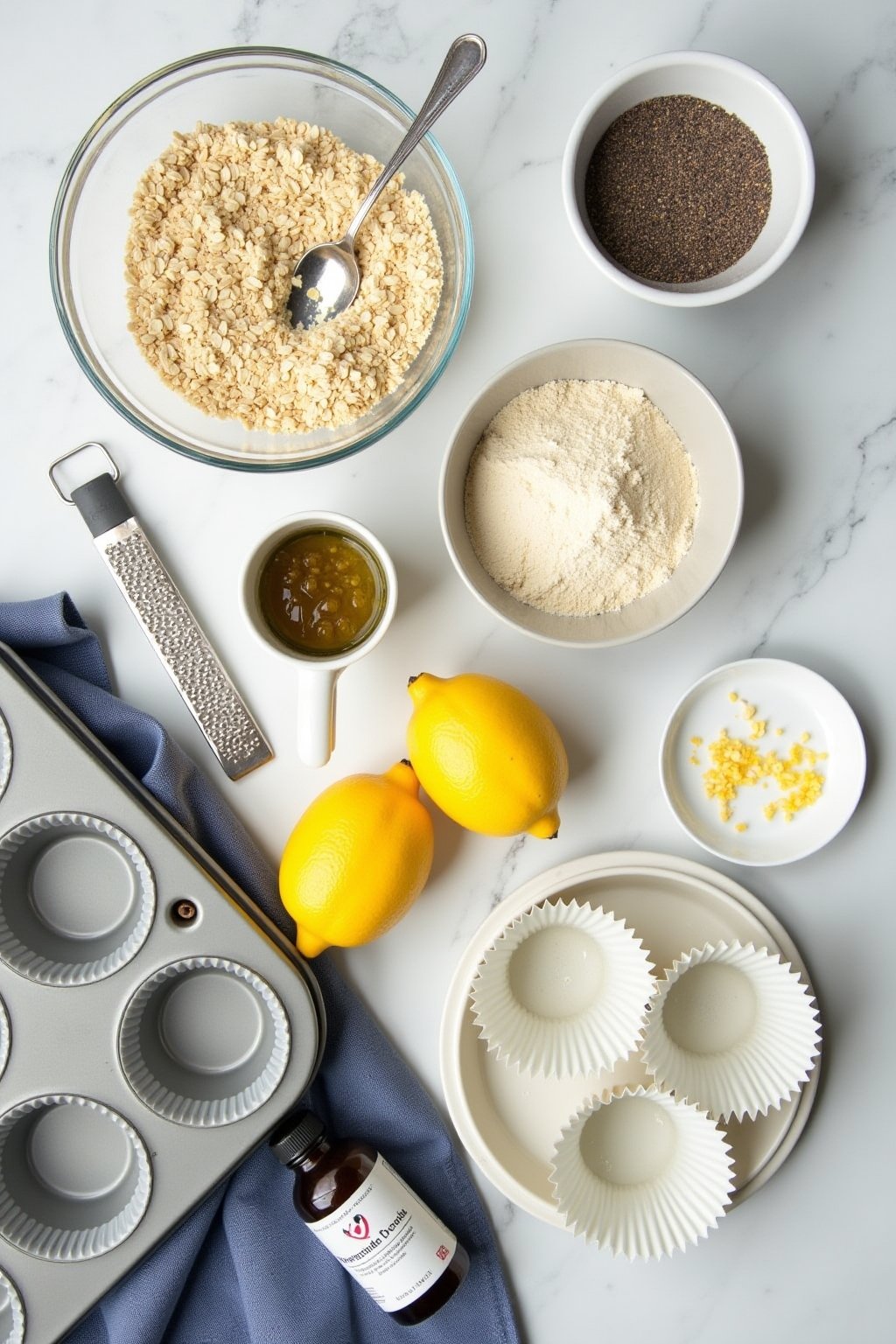 Overhead flat lay of chia seed lemon muffin ingredients: a bowl of almond flour, a small bowl of oat flour, chia seeds in a dish, two whole lemons and a microplane grater with zest, a small jar of ...